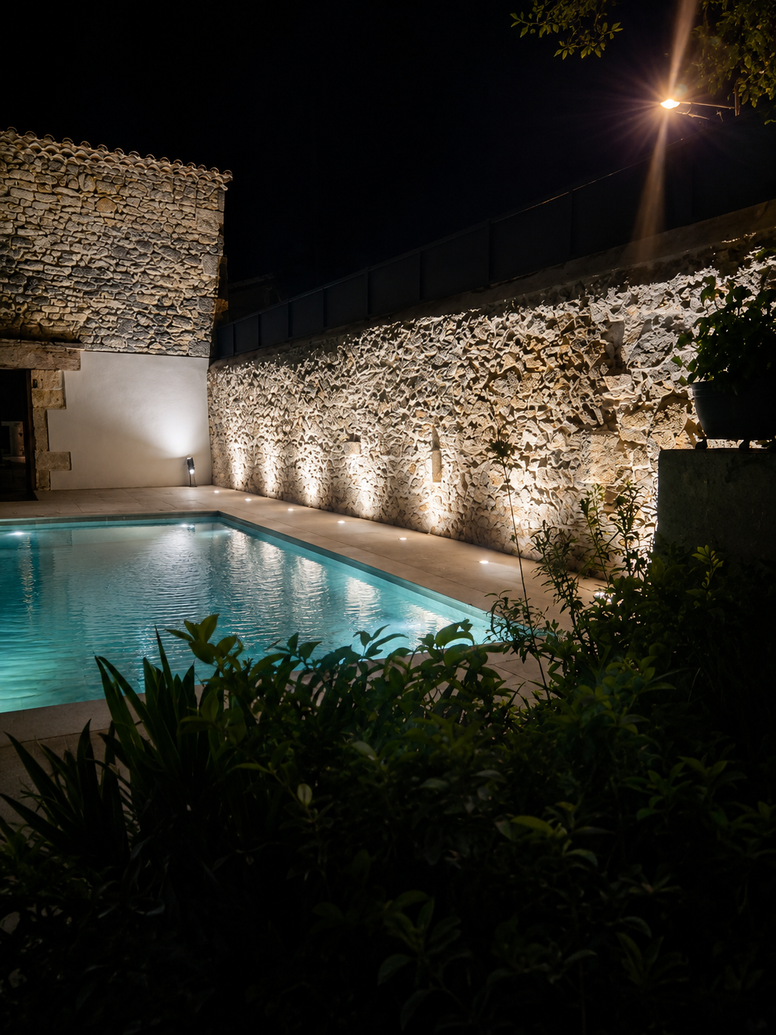 Piscine éclairée la nuit avec muret en pierre et éclairage au sol